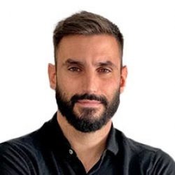 A man with short brown hair and a beard, wearing a black collared shirt, stands against a plain white background, ready to discuss bridge design and modeling.