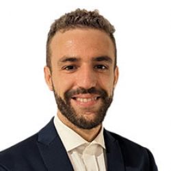 A man with short curly hair and a beard, wearing a dark suit and white shirt, smiles at the camera against a plain white background, reflecting the confidence of an expert in bridge design.