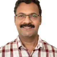 A man wearing glasses, a plaid shirt, and a mustache smiles warmly against a plain white background, reminiscent of an engineer who finds joy in the intricate world of roads and hydrology.