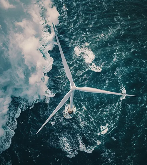 Aerial view of an offshore wind turbine surrounded by ocean waves and churning water.