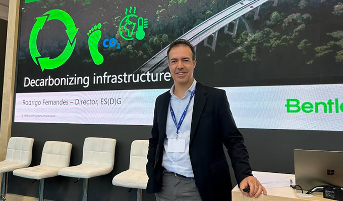 A person standing in front of a presentation slide titled "Decarbonizing infrastructure" with icons of recycling, a footprint, CO2, and Earth.